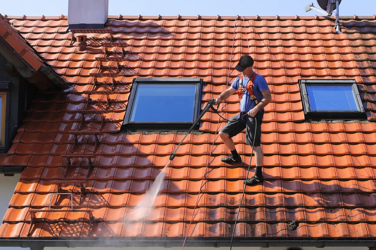 Roof cleaning specialist using pressure washer to remove algae and debris from slate roof in Troy, NY